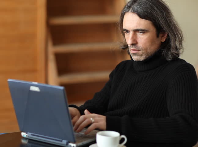 The man works on the computer and drinks coffee 