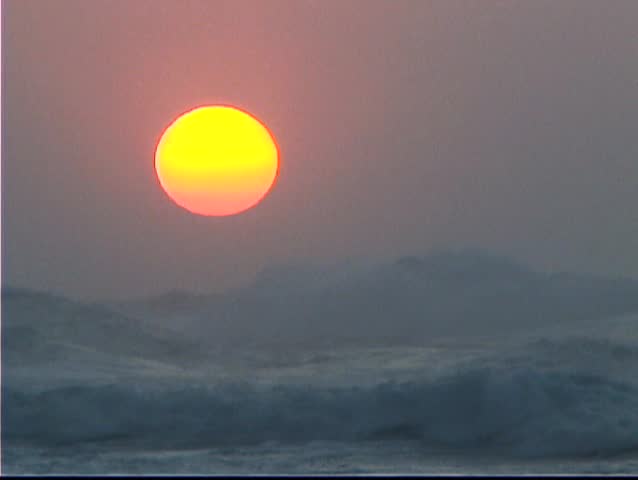 Big muted sunset with waves breaking in the foreground. This video was taken at the end of the road on Kauai, Hawaii on a big wave day.