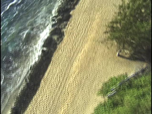 Aerial footage of a long stretch of beach in Hawaii. This beach goes on and on and the clip captures a unique angle that is a medium shot straight  down on the endless sand and surf.