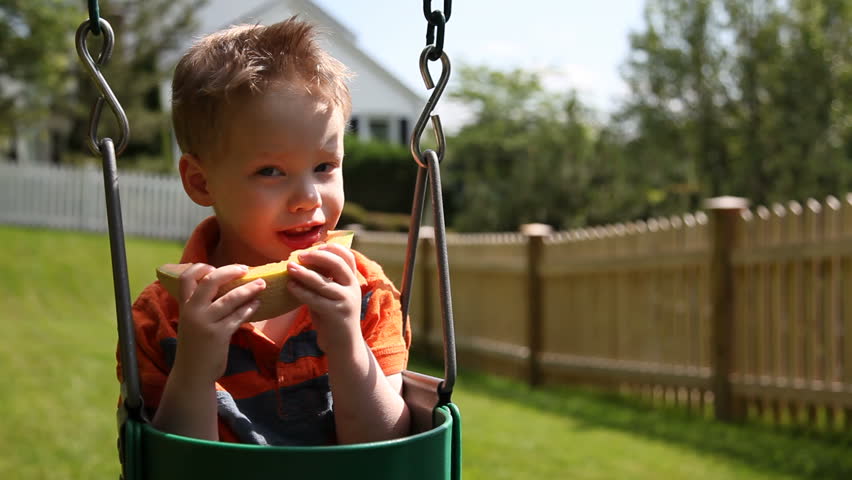 Young boy eating melon on swing