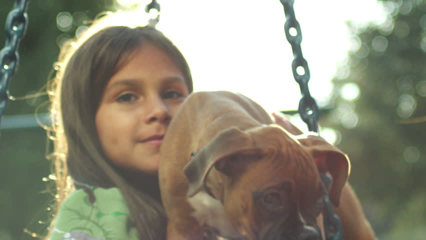 Little girl holds puppy on a tire swing. Medium shot.
