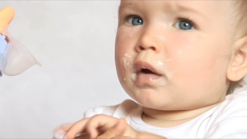 Baby sits at a children's little table. Mum gives to drink water of the child. Isolated on the white.