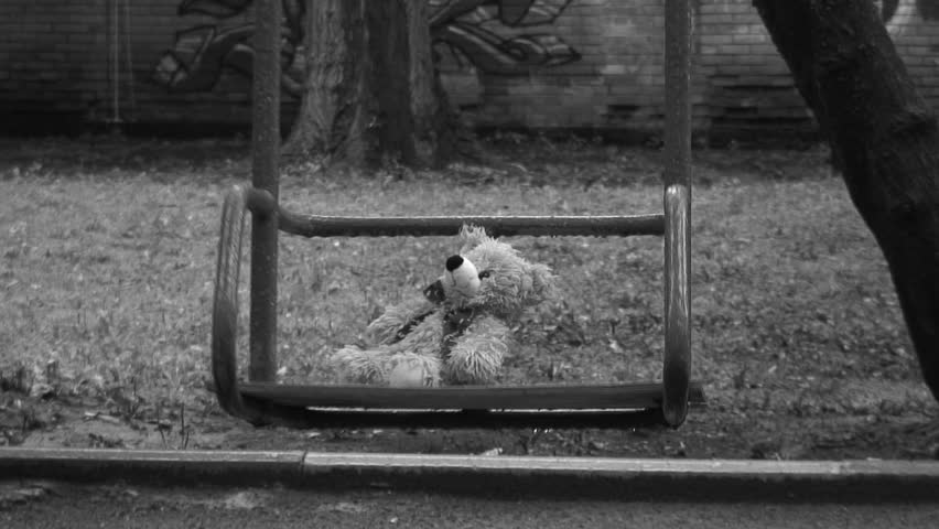 Forgotten Teddy bear on a swing under rain. Deep depression theme. Black and white.