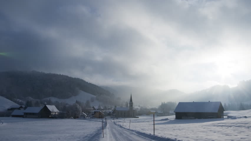 A moving holiday season winter postcard: A small village with church in the snow, clouds pass by. 