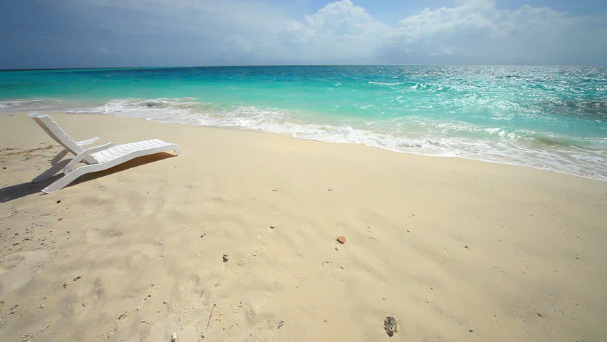 Unoccupied lounge chair wait for someone to sit in them on a sun drenched tropical beach. 
