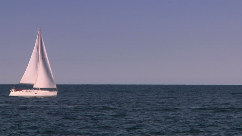 Sailboat sails on a lake in the summertime framed by a perfect horizon.