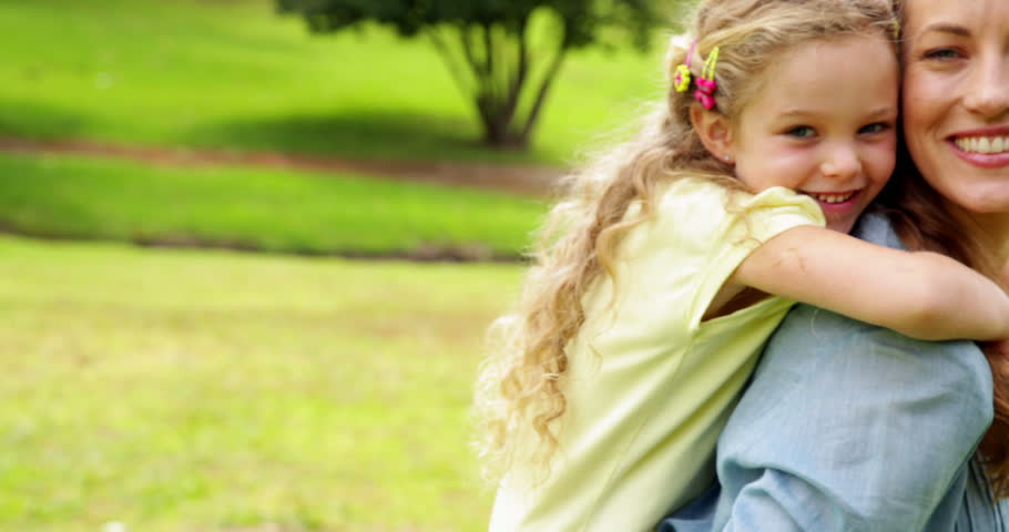 Happy mother giving her daughter a piggy back on a sunny day