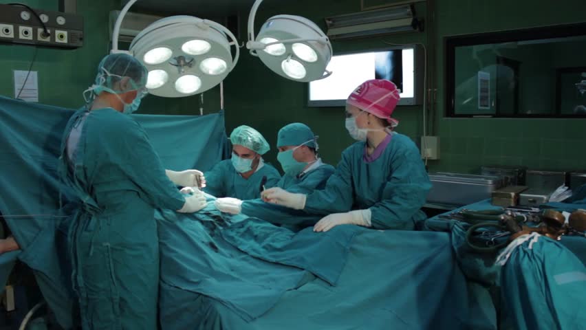 Surgeons Team Performing Operation In Hospital Operation Room Nurse Adding Surgical Tools Needle