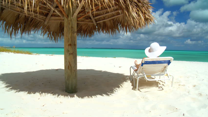 Elegant young female relaxing on a stunning white sandy beach looking at aquamarine waters