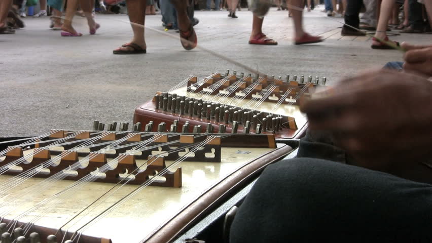 Two Asian teenagers play the Khim as onlookers walk by on the streets of Bangkok, Thailand.