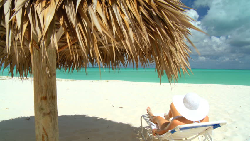 Elegant young female relaxing on white sandy beach looking at aquamarine waters
