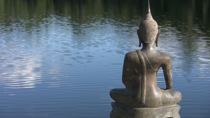 Buddha by the lake. A seated statue of Buddha sits by the lake. Space for text on left side.