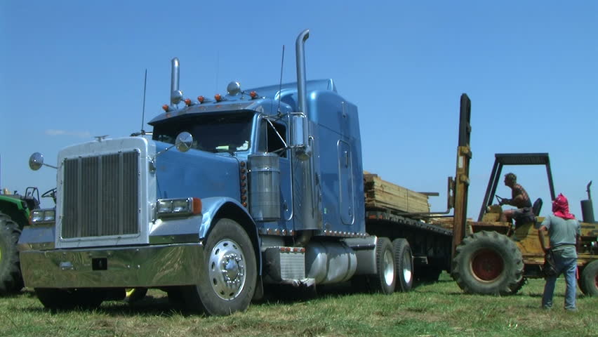 Worker operates forklift to unload truckload of lumber on construction site. 