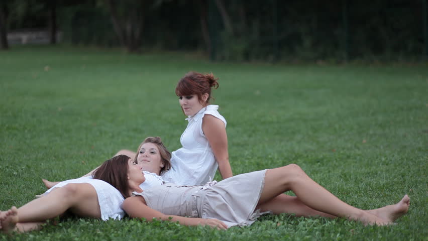 HD footage of three beautiful young female college students lying on the grass outdoors on a campus, chatting, laughing, having a great time