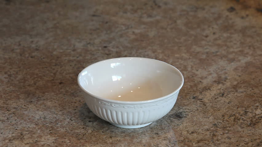 Cereal Corn Flake cereal being poured into a bowl slow motion. Breakfast meal. Pour into white bowl. Bowl sitting on polished granite counter. 