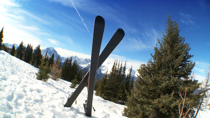 Crossed carver downhill skis & poles standing in fresh clean snow high in scenic mountain landscape