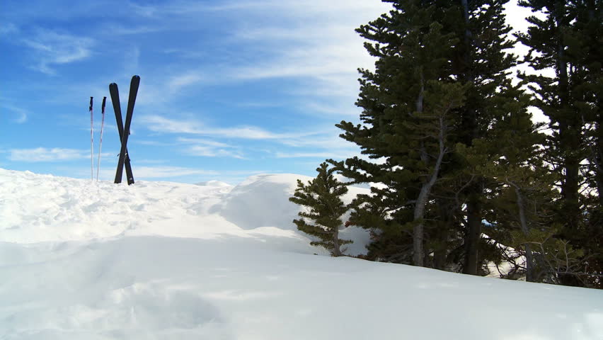 Crossed carver downhill skis & poles standing in fresh clean snow high in scenic mountain landscape