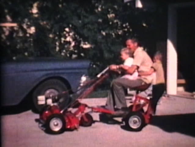 A loving dad takes his two young children on a fun adventure riding on his new riding lawn mower.