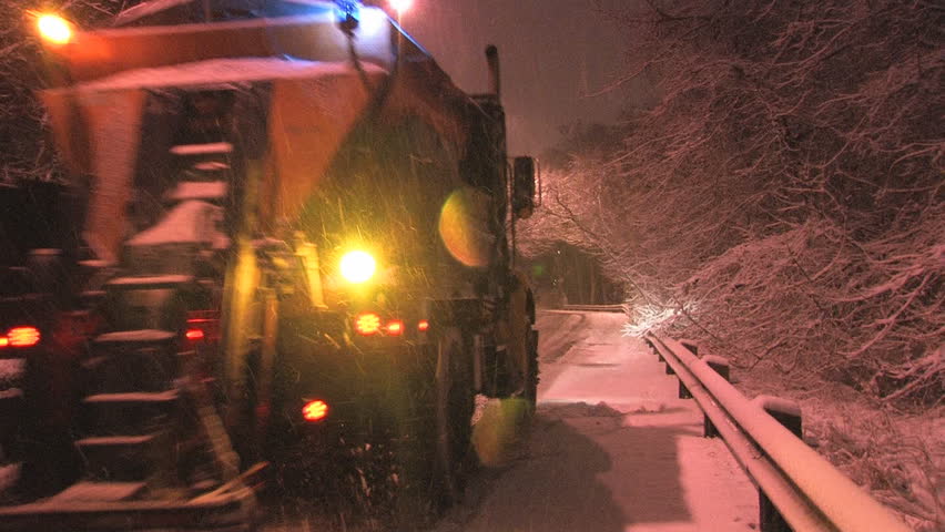 Salt truck driving up a steep hill, laying salt on a snowy, city street. Snowstorm at night in Toronto, Ontario.