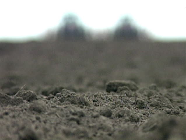 Rack focus shot of tractors in the far and the soil in the first plan, from the lower angle of camera.