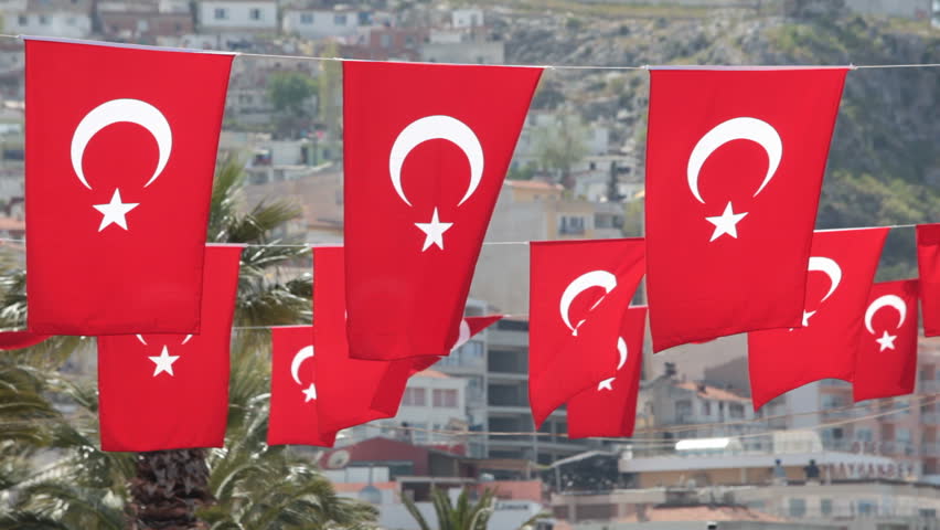 Close up of small red Turkish flags as bunting with white Crescent Moon and  Star hanging sideways and blowing in the wind