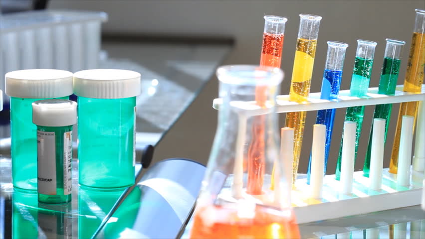 The camera dollies past laboratory or pharmacy paraphernalia such as test tubes, empty pill bottles to a large microscope.