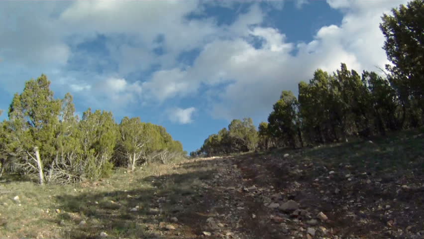 AtV climbing a steep and rock trail up the side of a mountain. First person view with shadow of machine. Shot from moving vehicle.