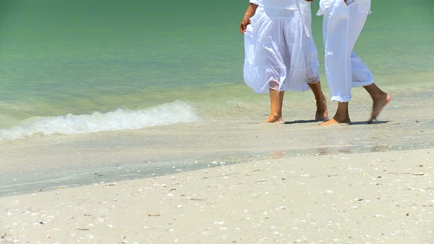 Legs & feet of senior couple having fun splashing barefoot in the shallows on the beach 60FPS