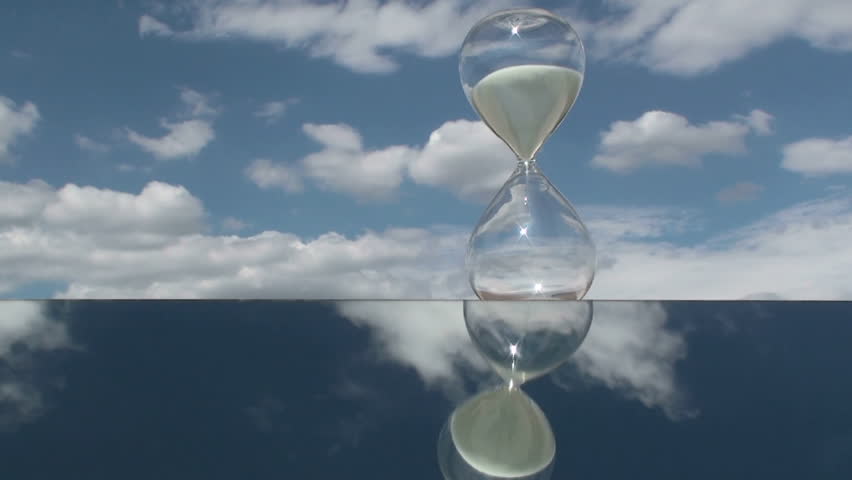 Time lapse, Sand slips through hourglass amid fast moving clouds. 