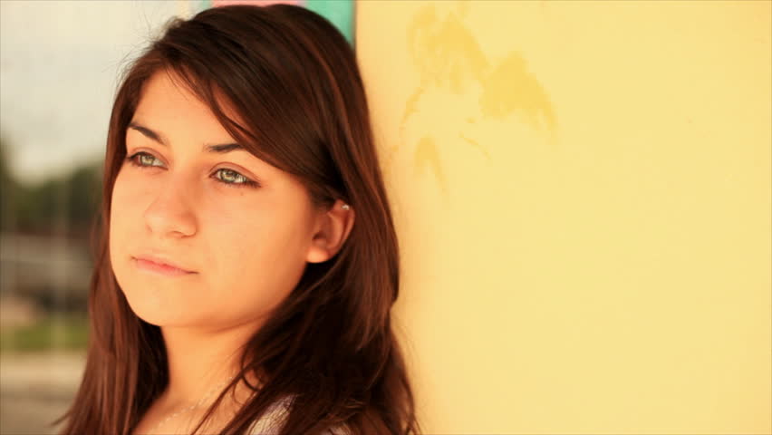 A beautiful brunette girl with piercing eyes gazes at the camera as she leans against a colorfully painted wall.