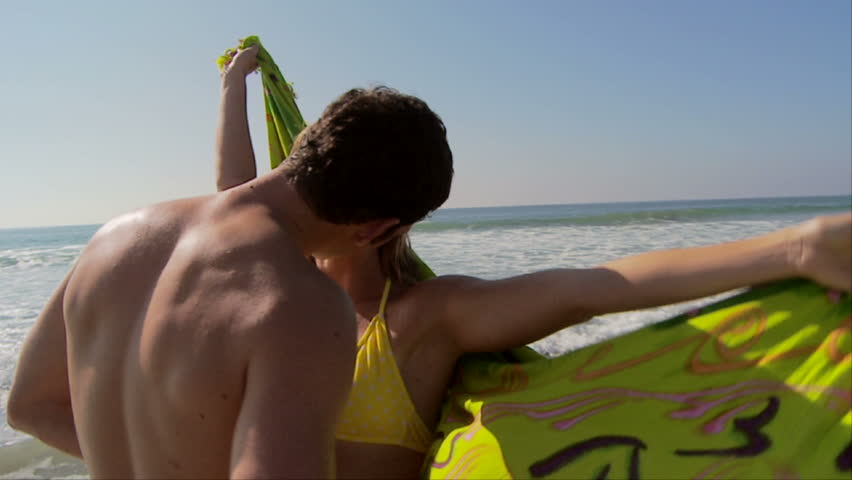 Young couple kissing at ocean's edge with scarf blowing in breeze