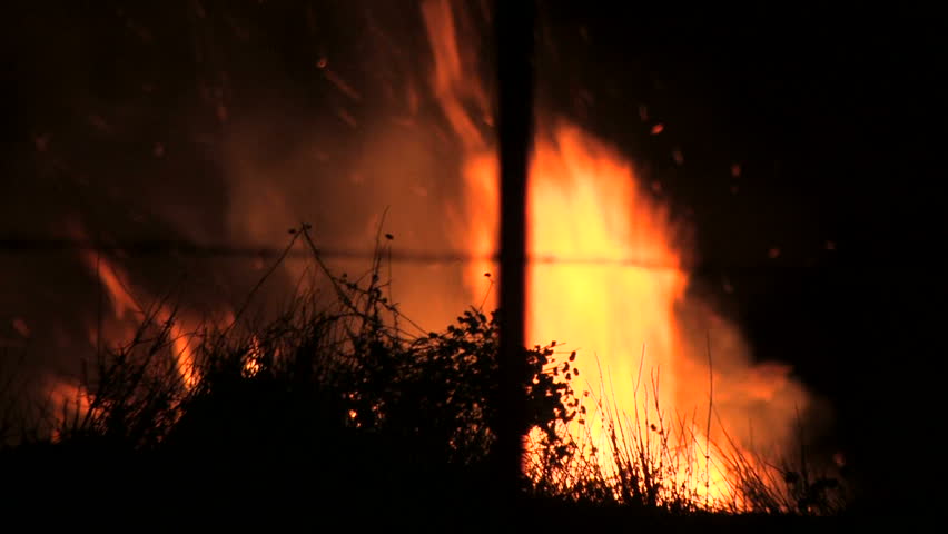 During a California wildfire, brush is consumed by fire. The blaze grows as firemen rush to save homes. You can hear a bulldozer nearby clearing the hillside.