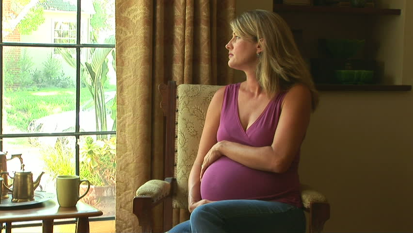 Portrait of pregnant woman by window caressing her belly