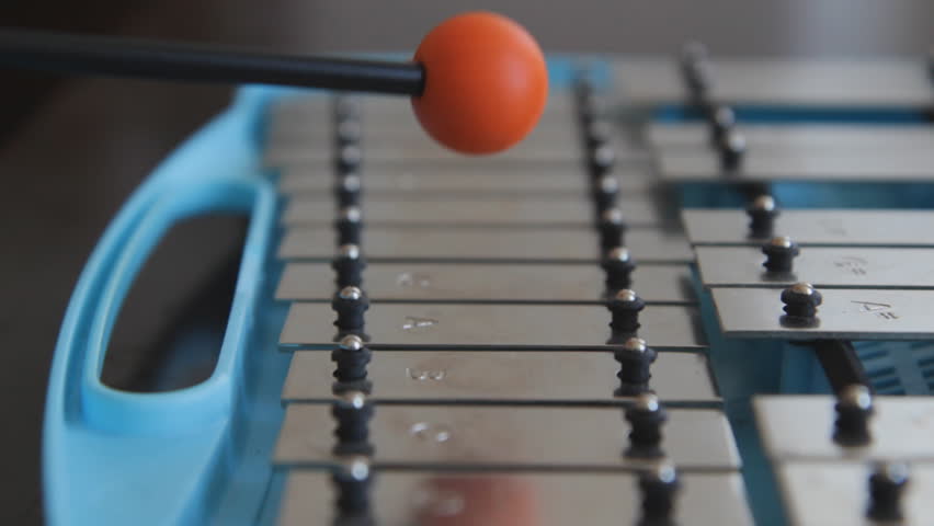 Glockenspiel. Playing a blue children'?s glockenspiel with an orange rubber mallet. Closeup and shallow DOF.
