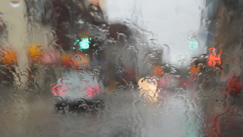Rainy intersection with pedestrians. View through wet windshield of intersection with pedestrians crossing. 