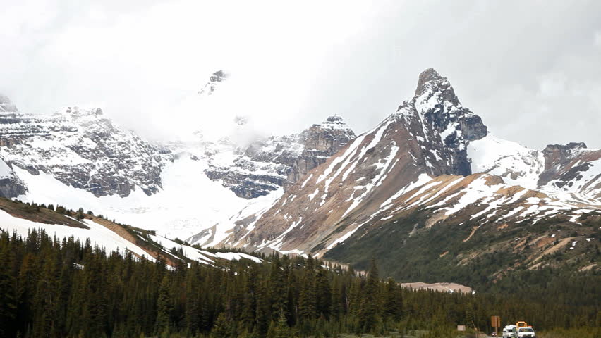 Snow fields along the ALCAN Highway in Jasper National park, Canada. Traffic driving towards view. Mountain peaks hidden by fog and clouds. Beautiful forest and glacial ice in summit.