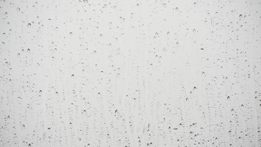 Close up of a window with rain drops falling down.