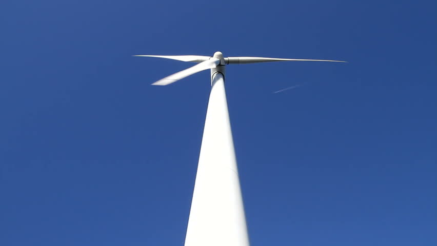 White wind turbine rotating at full force on a clear blue day