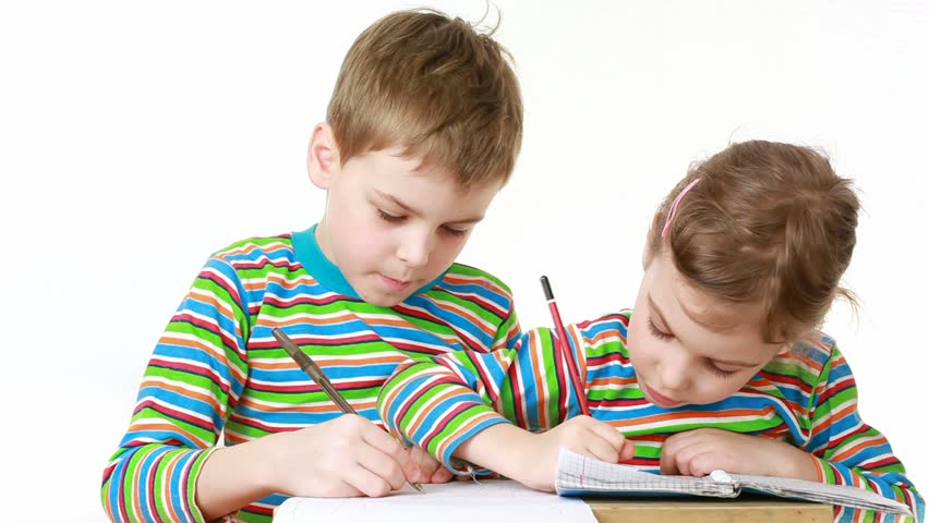 Little girl in a striped T-shirt with long sleeves and little boy in exactly T-shirt with a chocolate-smeared mouth draw pictures in notebooks, sitting at desk