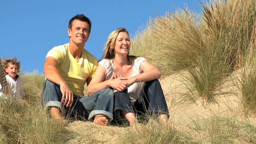 Attractive young caucasian family enjoying outdoor time together on coastal sand dunes  filmed at 60FPS