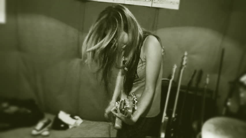 Rock and roll time. A girl with long hair is actively playing a guitar. Old movies. Hand held camera. 