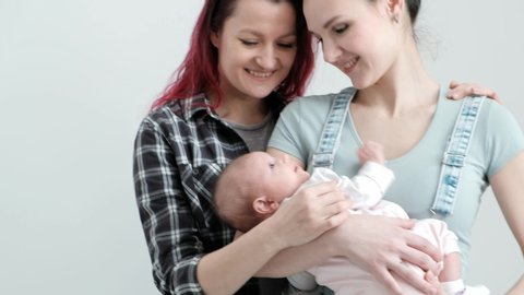 Two young women with dyed red hair and in casual clothes with a baby on a  white background. same-sex marriage and adoption, homosexual lesbian couple.