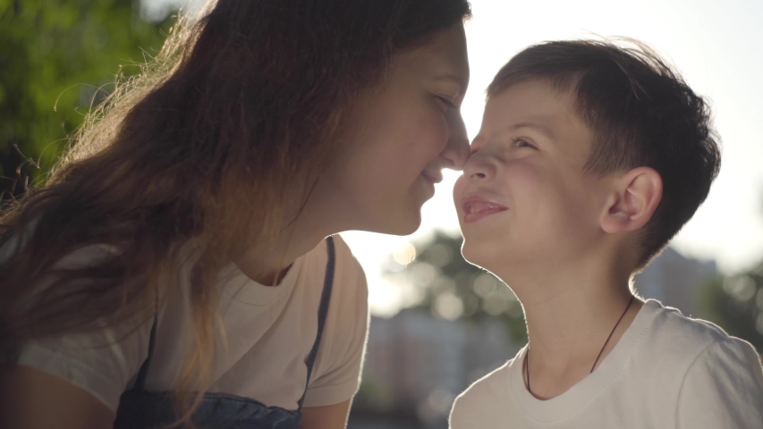 Older sister younger brother. Siblings Kiss. Portrait of older sister spending time with younger brother. Portrait of a little brother and little sister Stand and Touch nose to nose each other. Young brother and sister nose to nose in a Park, Side view.