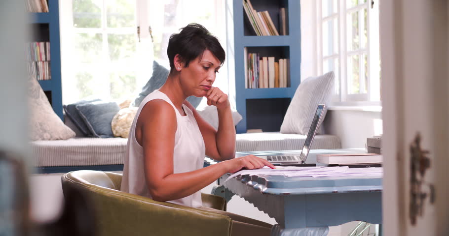 Working In Home Office worried man sitting at desk in home office looking at laptop stock Working In Home Office worried man sitting at desk in home office looking at laptop stock