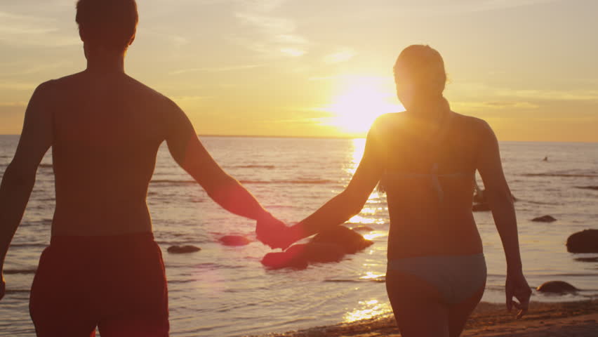 Happy Couple Holding Hands And Walking Away From Camera Into The Sunset ...