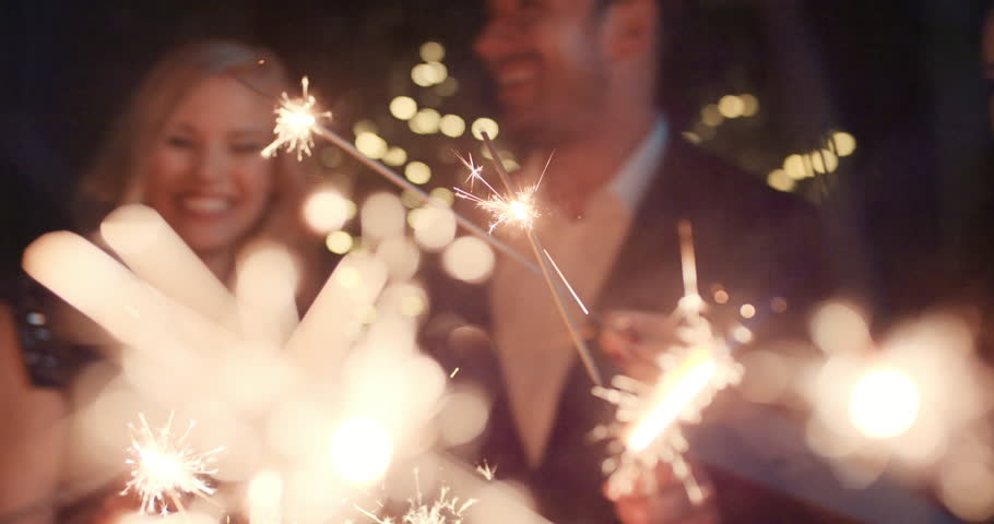 Sexy happy group of friends at glamorous party lighting sparklers having fun smiling celebrating new year's eve.
