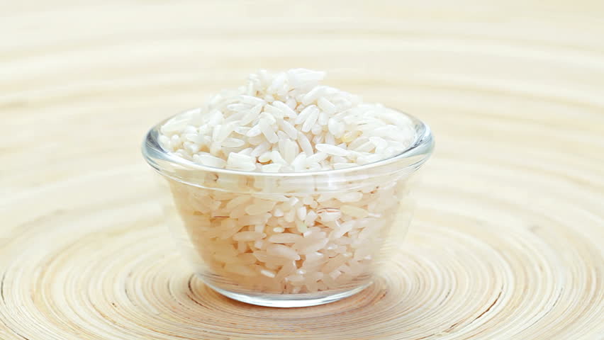 polished long rice heap in a glass bowl rotating on wooden plate