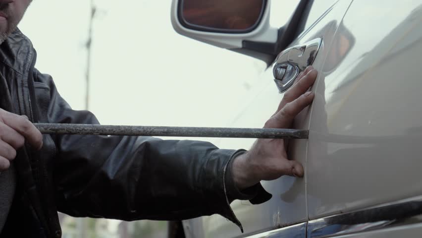 Car Thief Using A Pry Bar To Open The Door Of A Car