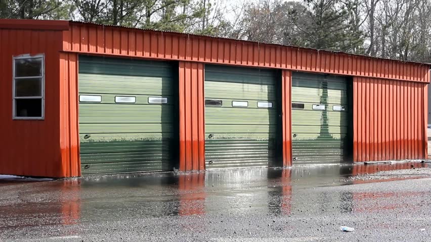 Two Old Green Garage Doors And Red Metal Building Gets Wet From Old Red Metal Building With Three Green Garage Doors Trees Ing In Background And Water