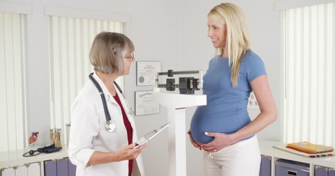врач измеряет вес беременной женщины на приёме